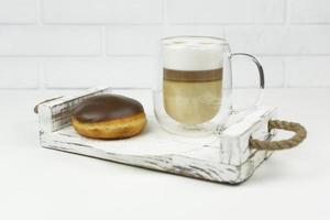 A cup of latte and a glazed donut lie on a wooden tray for early breakfast photo