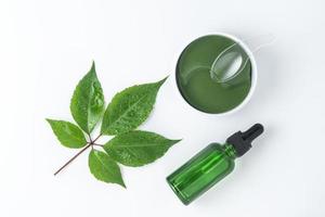 A green face serum or essential oil made of grapes and eye antiaging patches lying on a white background photo