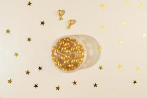 A face antiaging serum or essential oil in golden capsules and a wooden guasha massager as a present for Christmas holidays lying on a beige background with bright yellow confetti stars around it photo