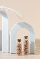 Two glass bottles with pink sea salt for spa procedures for face or body standing between geometric forms photo