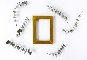 A golden frame for copy space and green leaves of eucalyptus around on a white background. Copy space photo