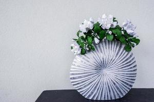 Flowers in a vase stands on the table as a part of the decor in the modern apartment. Textured white wall background photo