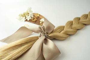 una trenza rubia con un lazo beige y vitaminas de aceite para el cabello, un peine de madera cerca foto