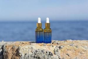 los frascos cuentagotas cosméticos se colocan sobre piedras a la orilla del mar con el mar al fondo foto