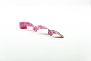 A pink measuring tape lies on a white table photo