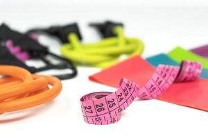 Colorful fitness elastic bands and expanders, a pink measuring tape lie on a white floor photo