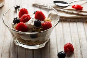 Raspberries, blueberries, cereals and yogurt in a glass bowl on wooden slats. Healthy breakfast for a healthy life. Horizontal image. photo