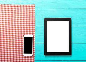 Electronic devices with place for text and red plaid tablecloth on blue wooden background. Top view and copy space. photo