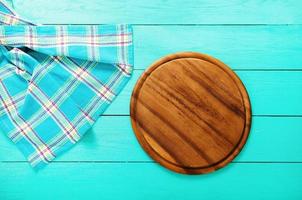 Plaid tablecloth and brown cutting board for pizza on blue wooden table. Top view and copy space. Mock up photo