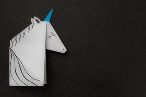 unicornio blanco realizado en la técnica del origami en el lado izquierdo de la foto sobre fondo negro. con lugar para tu texto