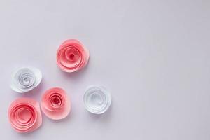 White and pink origami roses are scattered on a light background. With place for your design photo