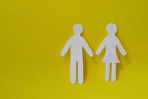 Silhouettes of a man and a woman are carved from white paper, standing side by side on a yellow background. With copy space. The concept of love, relationships, family photo