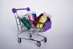 Mini decorative shopping cart with with colored threads for sewing on white background. photo