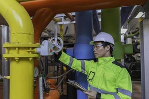 Asian engineer wearing glasses working in the boiler room,maintenance checking technical data of heating system equipment,Thailand people photo