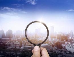 A man's hand holding a magnifying glass of the cityscape highlighting the business vision background photo