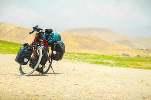 Loaded touring bicycle stands with moody dramatic panoramic mountains view and no cyclist photo