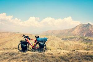 Loaded touring bicycle stands with moody dramatic panoramic mountains view and no cyclist photo