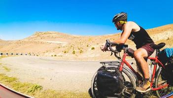 Male cyclist on cycling tour asphalt road stand alone outdoors with mountain panorama. Adventure travel outdoors. Before go uphill focus thoughtful. Determination and challenge photo