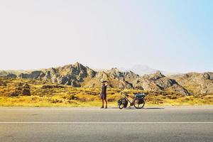 Cinematic travel inspirational panorama caucasian traveler cyclist stand on road take smiley self-portrait with mobile phone. Solo travel bicycle touring around the world photo