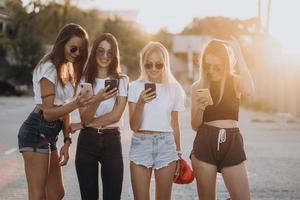 cuatro mujeres atractivas están de pie en el estacionamiento de automóviles con teléfonos inteligentes foto