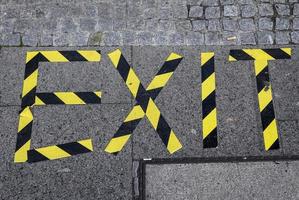 The word exit written with yellow and black barrier tape onto a sidewalk. photo