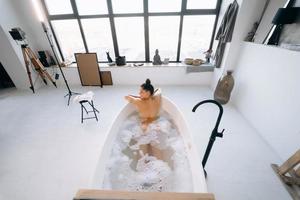 Relaxed lady taking bath, enjoying and relaxing while lying in bathtub, top view photo