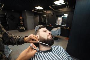 Hairdresser doing haircut of beard using comb and scissors photo