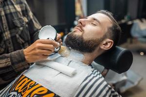 Master applying shaving foam on client face photo