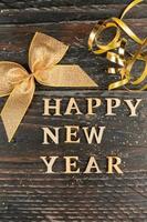 Happy new year wooden text decorated with golden bow and serpantine on wooden dark background. Festive greeting card for new year holidays photo