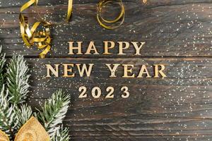 Happy New Year 2023. Quote made from wooden letters and numbers 2023 on wooden background dcorated fir tree branch with golden bow. Creative concept for new year greeting card photo
