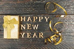 new year background. Wooden letters Happy New year, sequins, present box on a wooden background. Greeting card photo