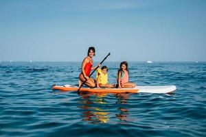 Mother with two daughters stand up on a paddle board photo