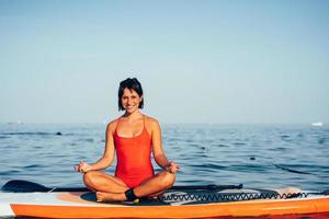 Young woman doing yoga on sup board with paddle photo