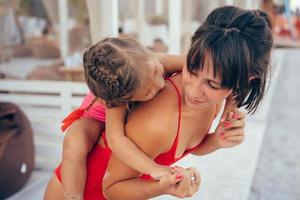 madre joven que da a su hija un paseo a cuestas en la playa foto