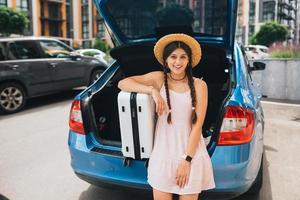 Woman packing her suitcase into luggage boot of the car. photo