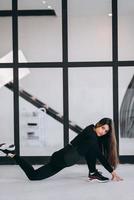 Young female wearing black sports suit exercising yoga pose indoors. photo