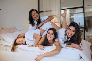 Positive young girls women friends indoors on bed at the hen party at home. photo