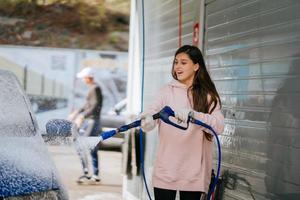 Brunette from a high-pressure hose applies a cleaner on the car photo