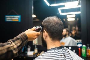 Master in barbershop makes men's haircutting with hair clipper photo