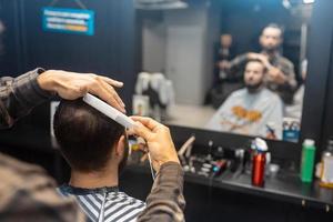 alegre joven barbudo cortándose el pelo por el peluquero en la barbería foto