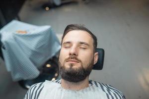 Handsome man with a beard and closed eyes in the barbershop. photo