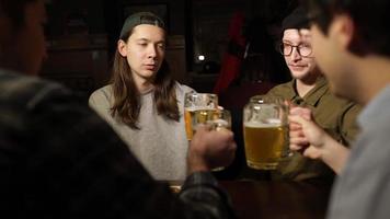 jóvenes amigos divirtiéndose juntos bebiendo cerveza y tintineando vasos en un pub. foto