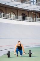 Young guy raises the bar in the stadium, outdoor workout photo