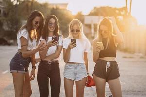 cuatro mujeres atractivas están de pie en el estacionamiento de automóviles con teléfonos inteligentes foto