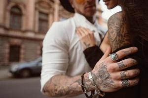 The man's hand in tattoos and jewelry embraces a girl's waist. photo