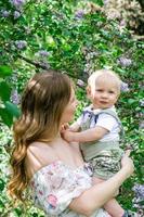 Portrait of young smiling mother with her little son in sunlight on background of blooming lilac trees. photo