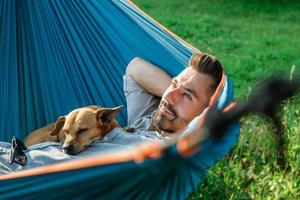 retrato de un atractivo hombre europeo en una hamaca con un lindo perro somnoliento. foto