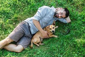 Smiling attractive European man is lying on grass and hugging his cute little dog. photo