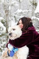 joven mujer sonriente está abrazando a su perro pastor del sur de Rusia en un fondo de bosque de coníferas de invierno. foto