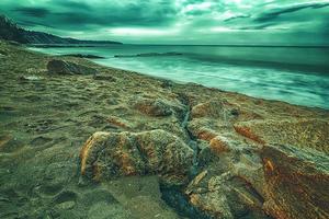 vista creativa del amanecer nublado con mar borroso y rocas en la playa foto